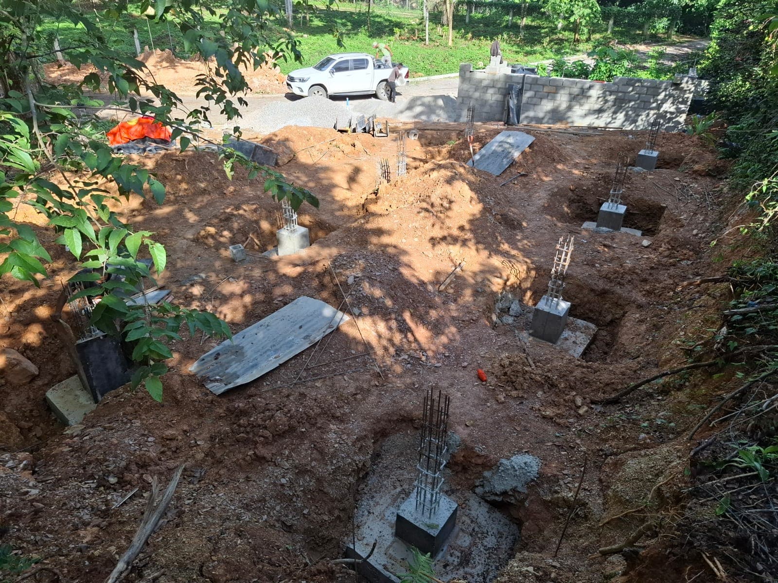 Multiple concrete column footings poured across the excavated plot, steel rebar rising from each